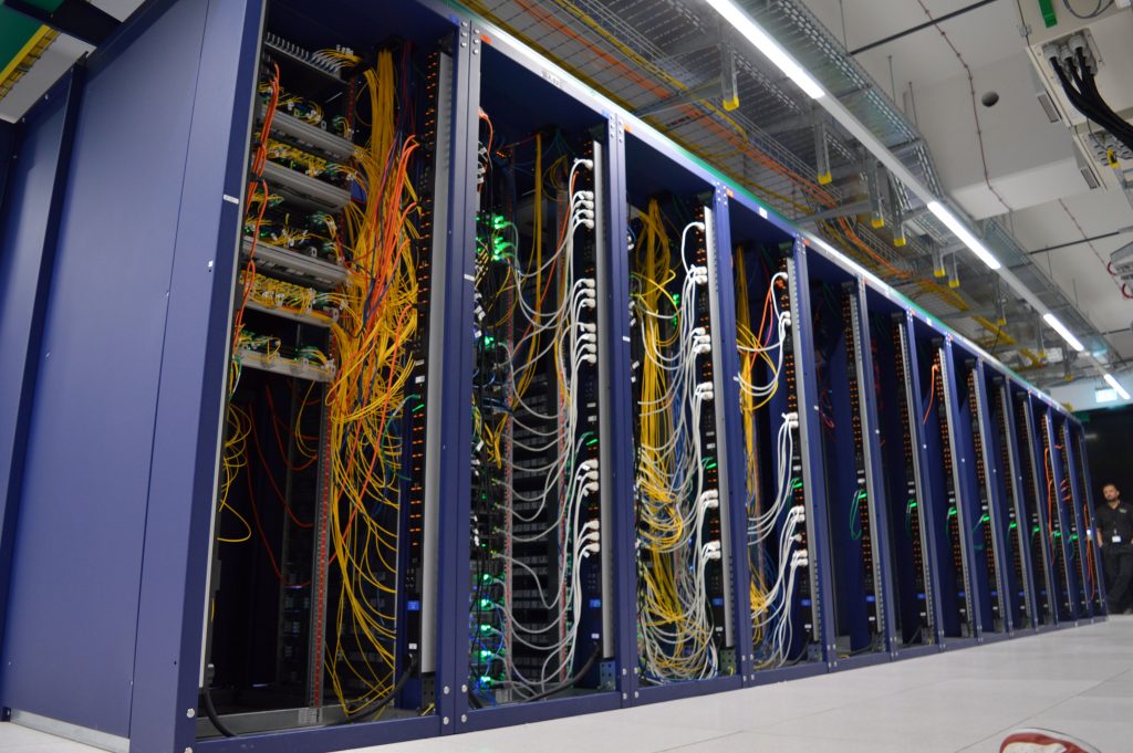 Nahaufnahme von mehreren aufgereihten Server-Racks in einem Rechenzentrum, mit installierten Servern und blinkenden grünen und blauen Status-LEDs.